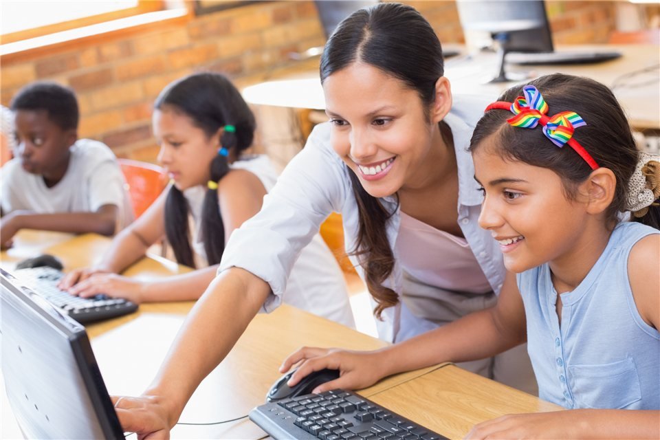 An educator helping children at classroom computers